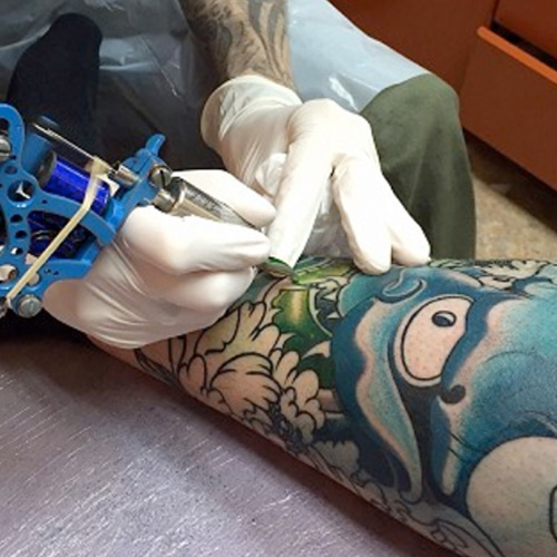 tattoo artist working on a japanese mask on a customers leg>